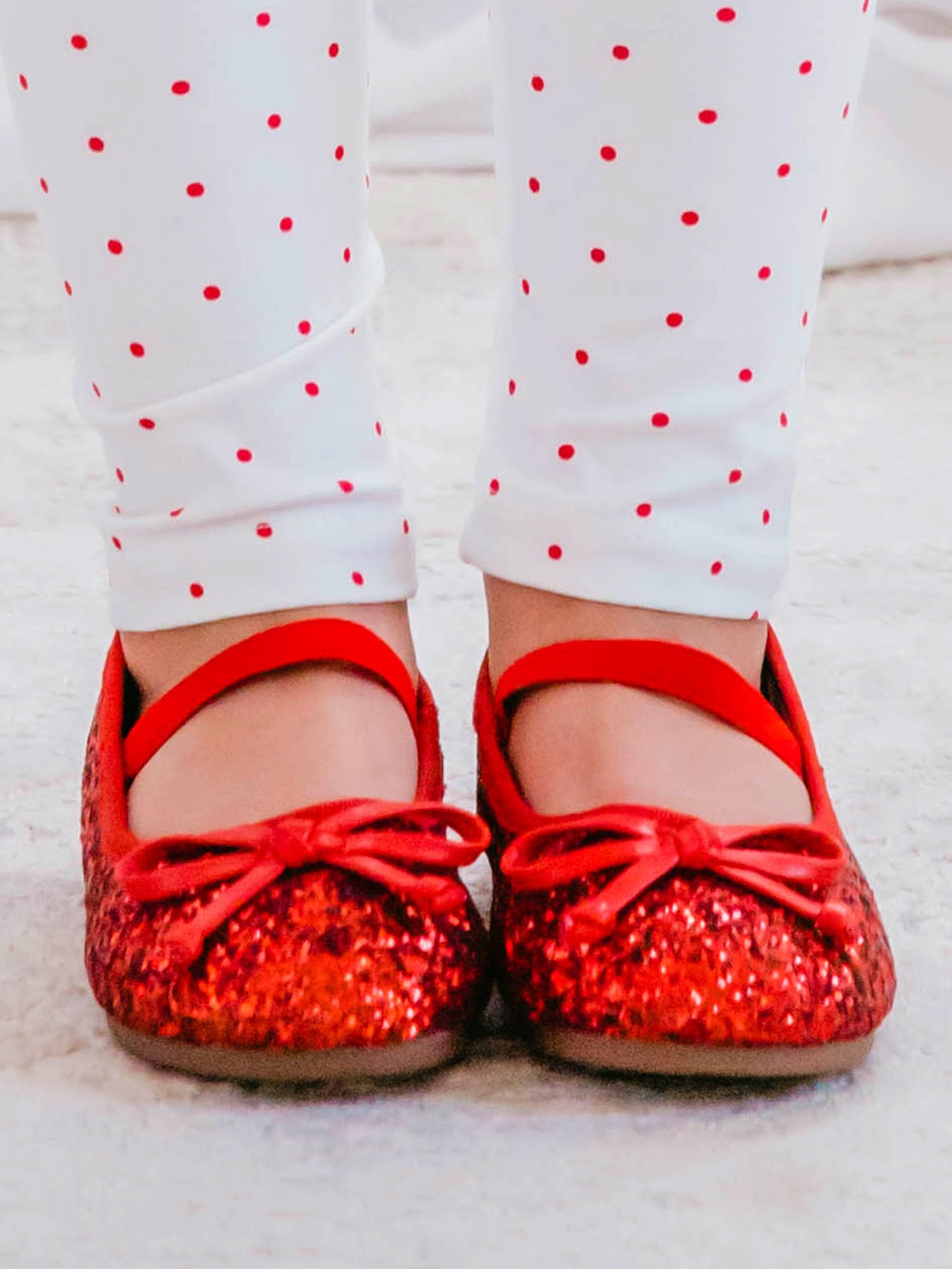 These Small Bow Glitter Ballet shoes come in red with an elastic strap across the top of the foot. The red bows bows are attached on top of the shoes’ toe.