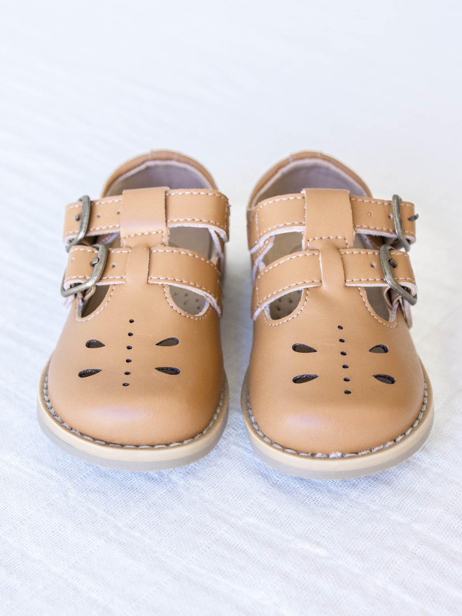 A pair of tan colored genuine leather rubber soled shoes with two adjustable metal buckles and cut out detail across the toe area in a dragonfly type pattern. 