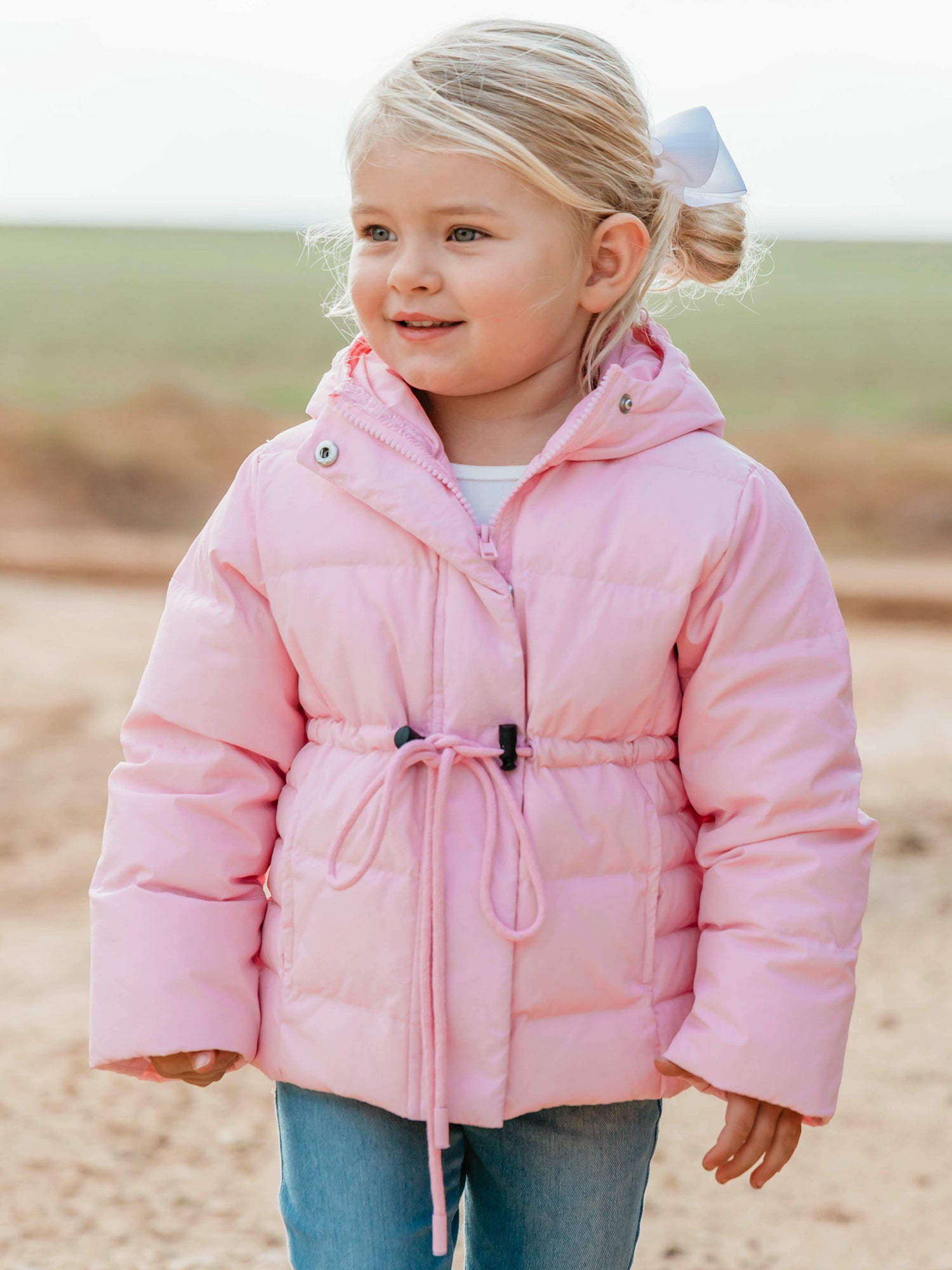 Keep her cozy and cute all season long in our Pink Puffer Jacket — the perfect blend of warmth and style! This soft, quilted jacket features a full zipper closure with a button placket, ensuring extra protection from chilly winds. Hidden front pockets keep little hands warm (or treasures tucked away), while the adjustable waist toggle allows for the perfect, comfortable fit. Designed in a beautiful blush pink hue, this girls’ puffer jacket pairs effortlessly with any winter outfit for a look that's fun!