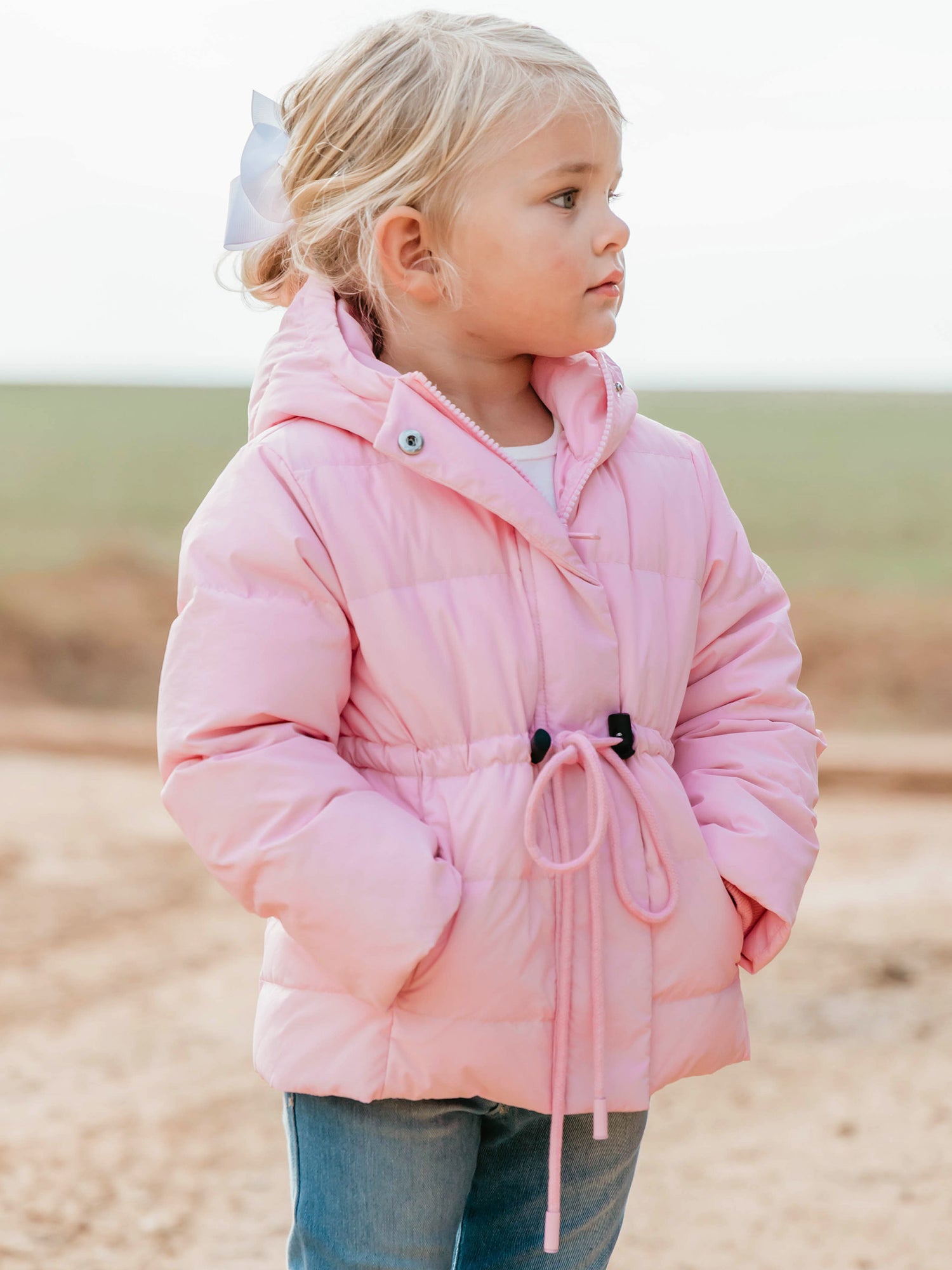 Keep her cozy and cute all season long in our Pink Puffer Jacket — the perfect blend of warmth and style! This soft, quilted jacket features a full zipper closure with a button placket, ensuring extra protection from chilly winds. Hidden front pockets keep little hands warm (or treasures tucked away), while the adjustable waist toggle allows for the perfect, comfortable fit. Designed in a beautiful blush pink hue, this girls’ puffer jacket pairs effortlessly with any winter outfit for a look that's fun!