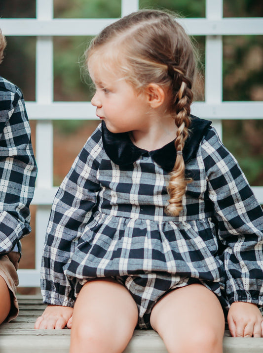 This image of a girl features the product Classic Bubble - Classic Girl. This Classic Bubble has a peter pan collar and buttons down the back. It is a black and white plaid pattern.