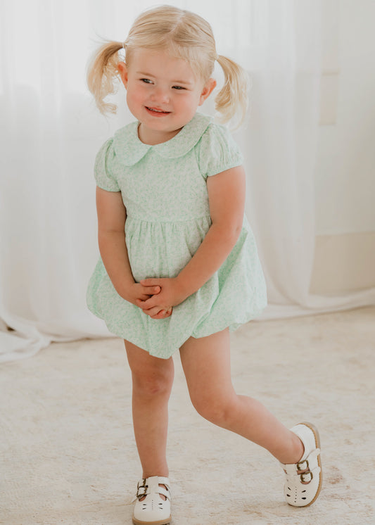 This image of a girl features the product Classic Bubble – Minty Petals. This Classic Bubble has a peter pan collar and buttons down the back. It is a pattern of dark mint line drawn flowers on a background of light mint.