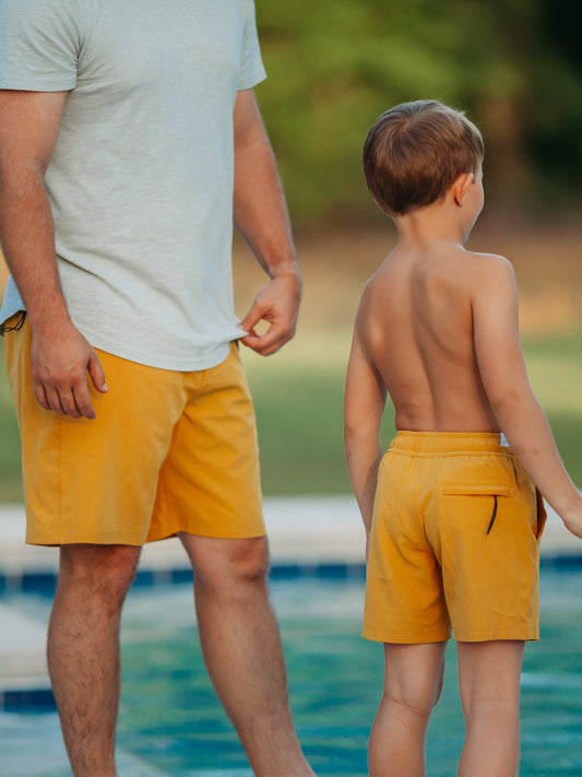 This image of a boy and his dad features the regular short style of our Boy's Everyday Lined Trunks – Yellow Solid