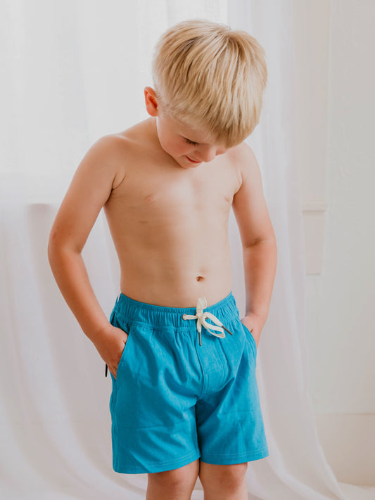 This image of a boy features the regular short style of our Boy's Everyday Lined Trunks – Aqua Blue Solid. 