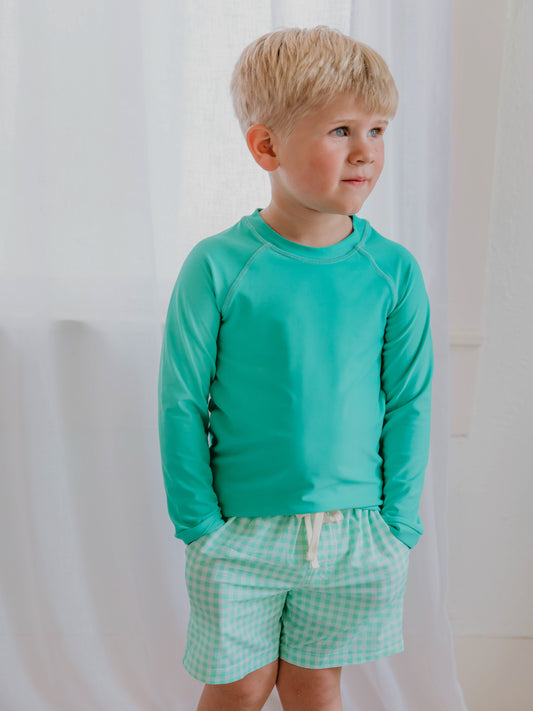 This image of a boy features the regular short style of our Boy's Everyday Lined Trunks – Green Check