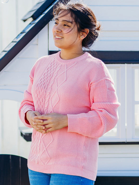 This image of a woman features the product Women's Cable Knit Sweater – Bright Pink. This crew neck sweater featuring a unique cable knit design down the middle.