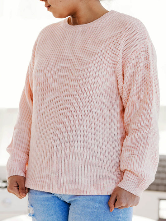 This image of a woman features the product Women's Knit Sweater – Light Pink. This crew neck sweater comes in a light pink color.